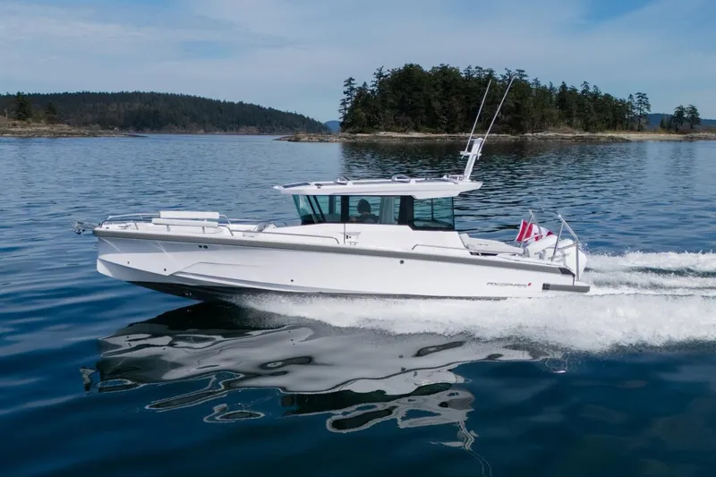 Slide: The Image of 2027 Axopar 29 XC Cross Cabin cruising on serene waters near a forested island. - 4
