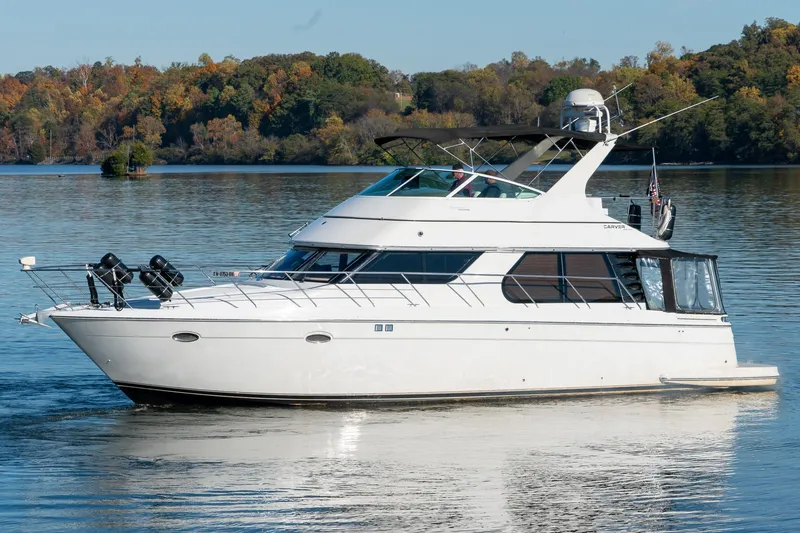 Slide: The Image of 2000 Carver 450 Voyager Pilothouse yacht on a serene lake with autumn foliage. - 1