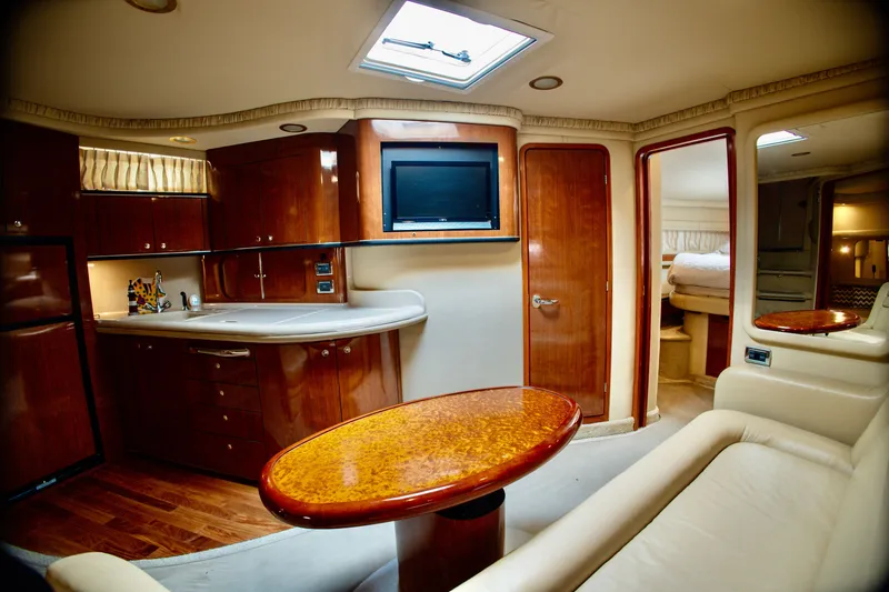 Slide: The Image of The interior cabin of a 2003 Sea Ray Sundancer 460 features an elegant kitchen, dining table, and cozy seating. - 17