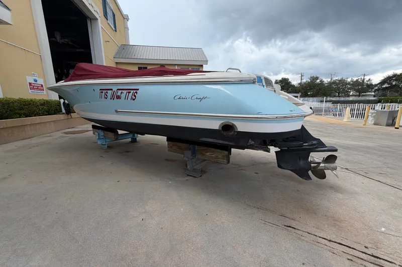 Slide: The Image of 2005 Chris-Craft Corsair 25 boat with red cover, parked outdoors on a cloudy day. - 11