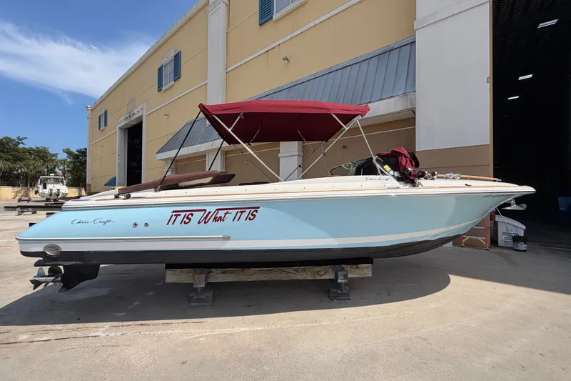 Slide: The Image of 2005 Chris-Craft Corsair 25 boat with red canopy, docked outside a warehouse. - 16
