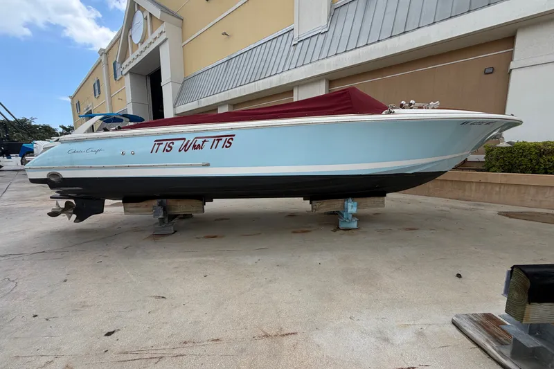 The Image of 2005 Chris-Craft Corsair 25 boat on dry dock, light blue hull, maroon cover. - 0