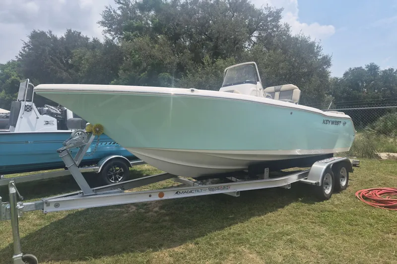 The Image of 2026 Key West 203 FS boat on trailer, parked on grass, surrounded by trees. - 1