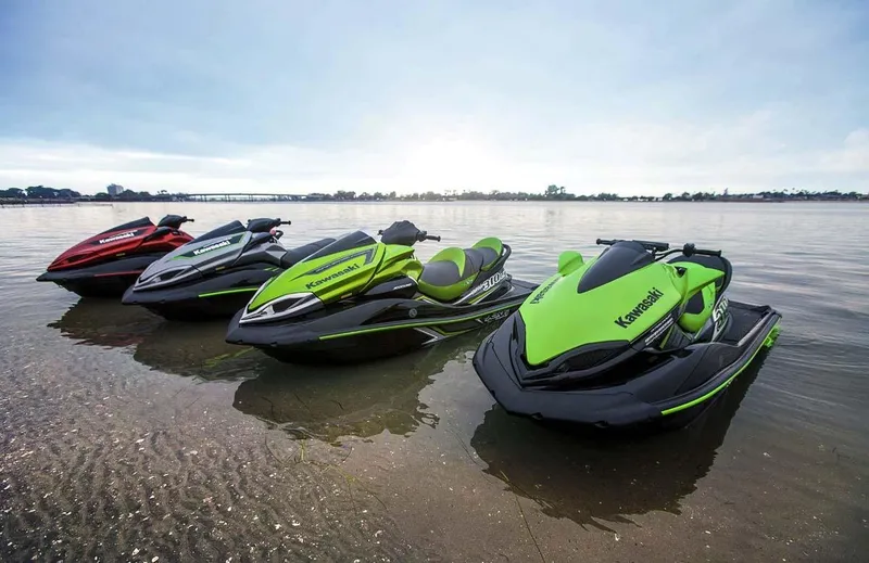 Slide: The Image of Three Kawasaki Jet Skis are lined up on the shore of a calm body of water. - 11