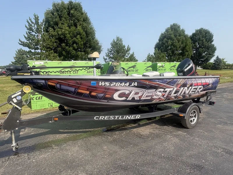 Slide: The Image of A 2014 Crestliner 1850 Fish Hawk on a trailer, surrounded by trees and green boxes. - 2