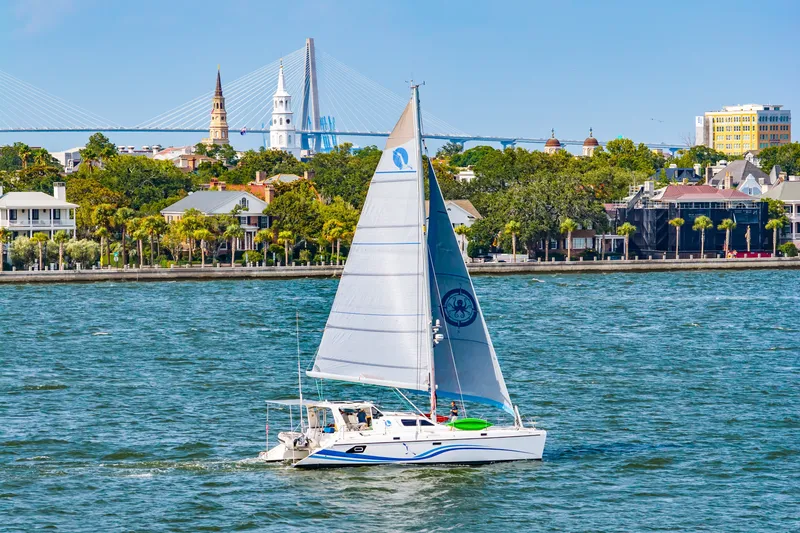Slide: The Image of Sailboat St Francis SF 50 cruising near a scenic waterfront with a bridge and historic buildings. - 0
