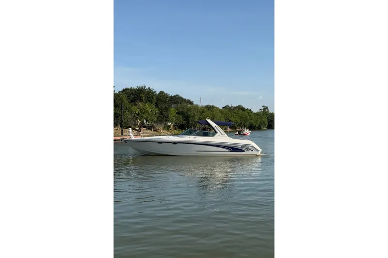 The Image of 2003 Formula 330 Sun Sport boat cruising on a calm lake under a clear blue sky. - 0