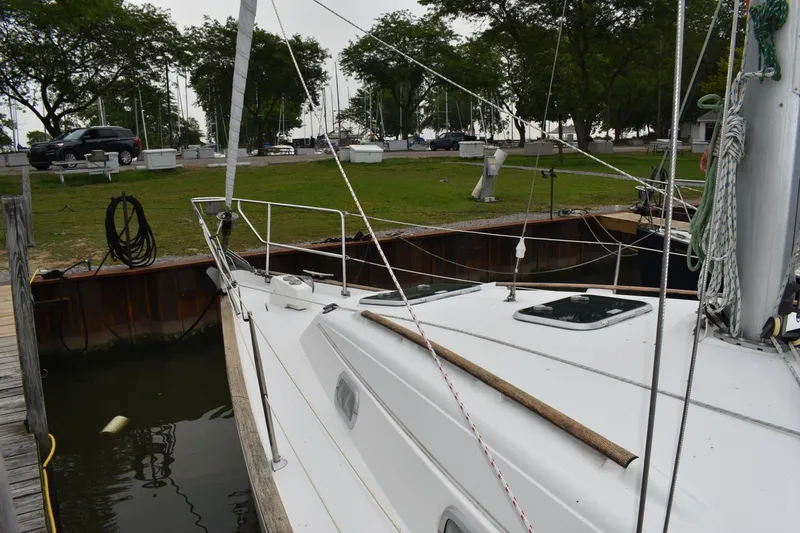 Slide: The Image of 1999 Beneteau Oceanis 36 CC sailboat docked, surrounded by greenery and parked vehicles. - 5