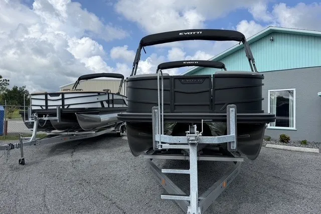 Slide: The Image of 2027 Evotti 523CS pontoon boats on trailers, parked outside a building under a cloudy sky. - 6