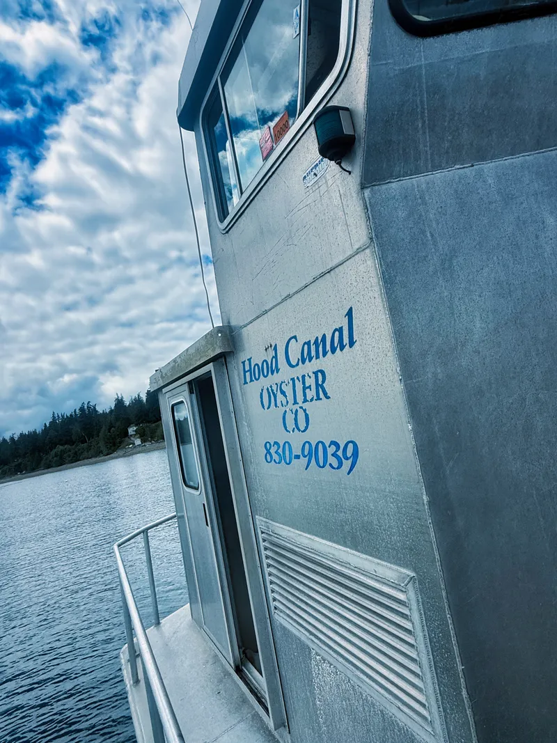 Slide: The Image of An aluminum boat with "Hood Canal Oyster Co" on the hull, floating on calm water. - 18