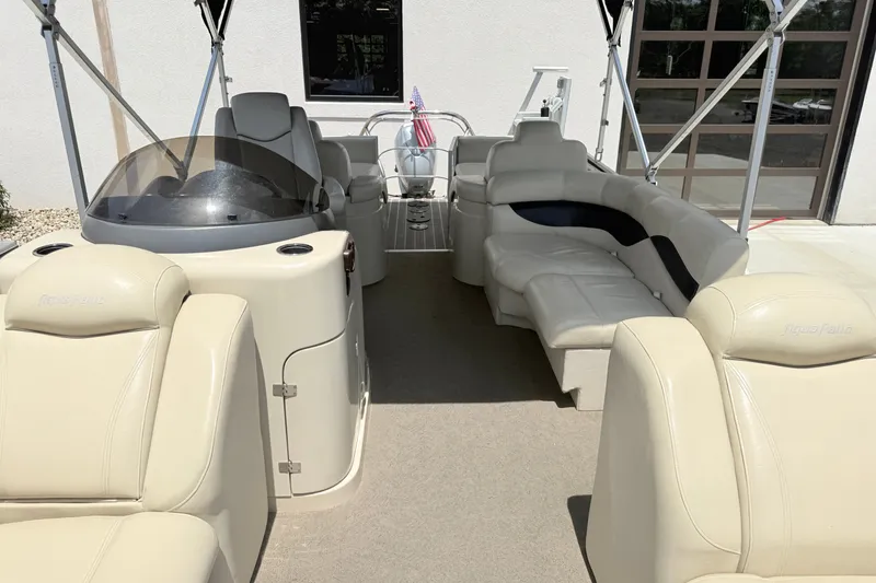 Slide: The Image of 2013 AquaPatio 240 RS boat interior with beige seating and helm, docked outdoors. - 12