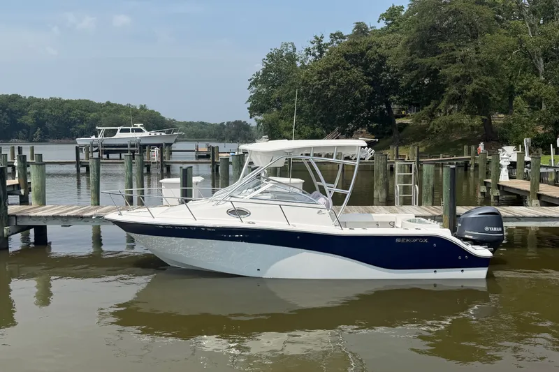 Slide: The Image of 2013 Sea Fox 256 Voyager boat docked at a marina with lush greenery. - 2
