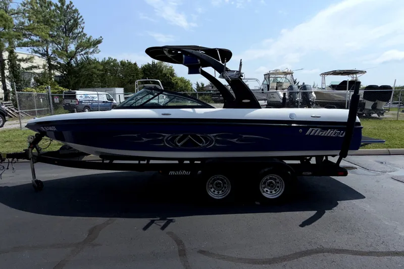Slide: The Image of 2008 Malibu iRide boat on trailer, parked outdoors with other boats in the background. - 4