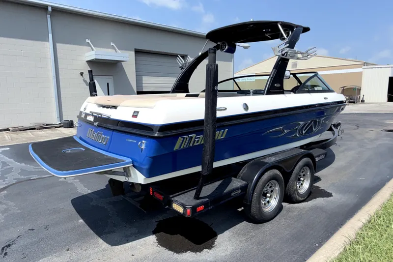Slide: The Image of 2008 Malibu iRide boat on trailer, blue and white design, parked outdoors. - 9