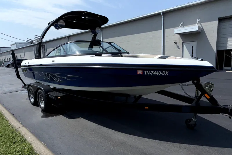 Slide: The Image of 2008 Malibu iRide boat on trailer, parked outside industrial building. - 2
