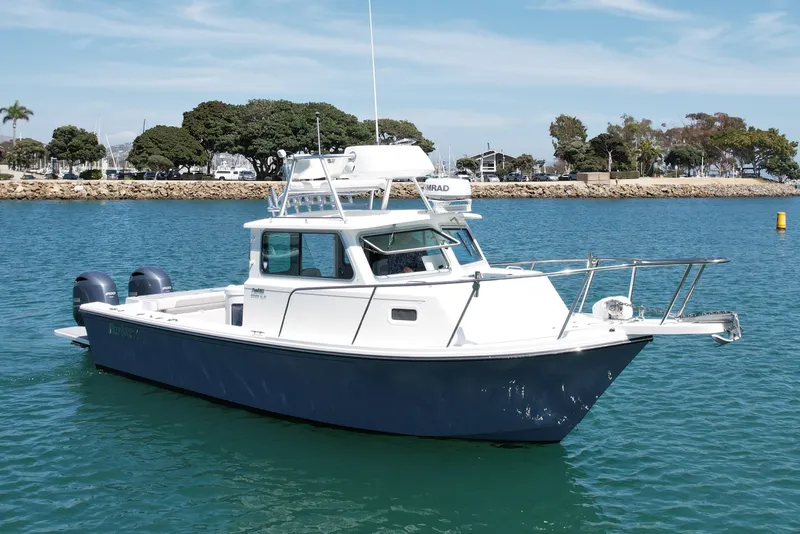 Slide: The Image of 2022 Parker 2520 XLD Sport Cabin boat on calm water, with scenic shoreline background. - 2