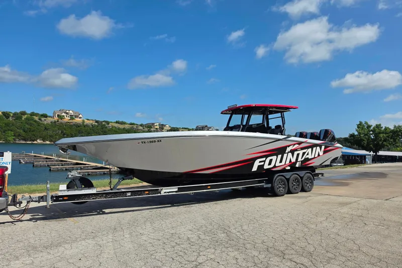 The Image of 2024 Fountain 38 SC boat on trailer by a lake under a clear blue sky. - 1