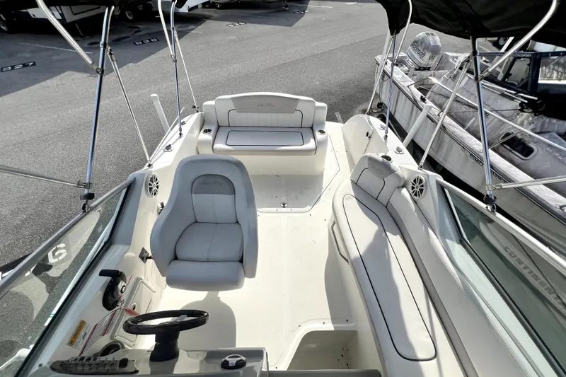 Slide: The Image of 2010 Sea Ray 240 Sundancer boat interior with seating and steering wheel, docked outdoors. - 43