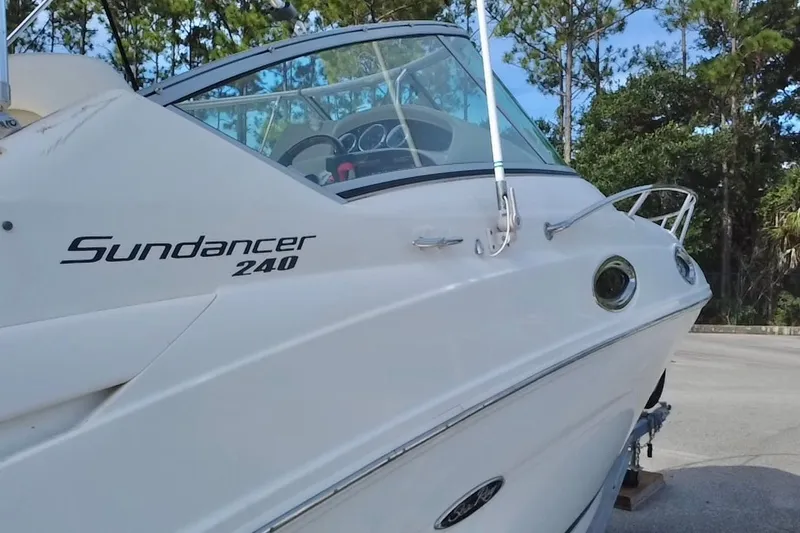 Slide: The Image of 2010 Sea Ray 240 Sundancer boat, side view, parked outdoors with trees in background. - 88