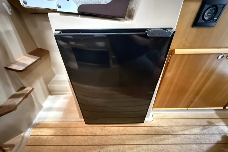 Slide: The Image of 2016 Cutwater C-24 interior with compact black refrigerator and wooden cabinetry. - 23