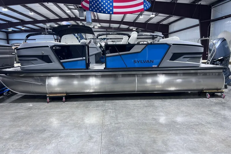The Image of 2026 Sylvan R-22 CLZ DH pontoon boat displayed indoors with American flag above. - 0