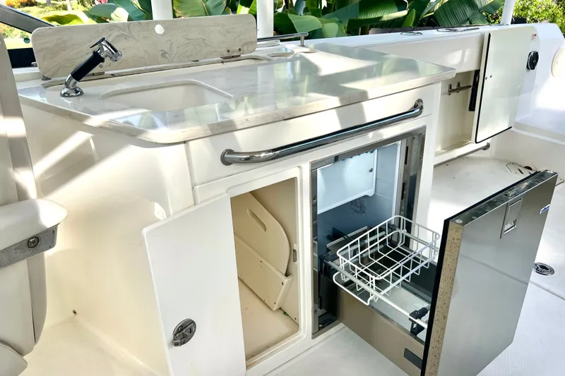 Slide: The Image of 2015 Boston Whaler 270 Vantage boat kitchen area with sink, storage, and refrigerator. - 64