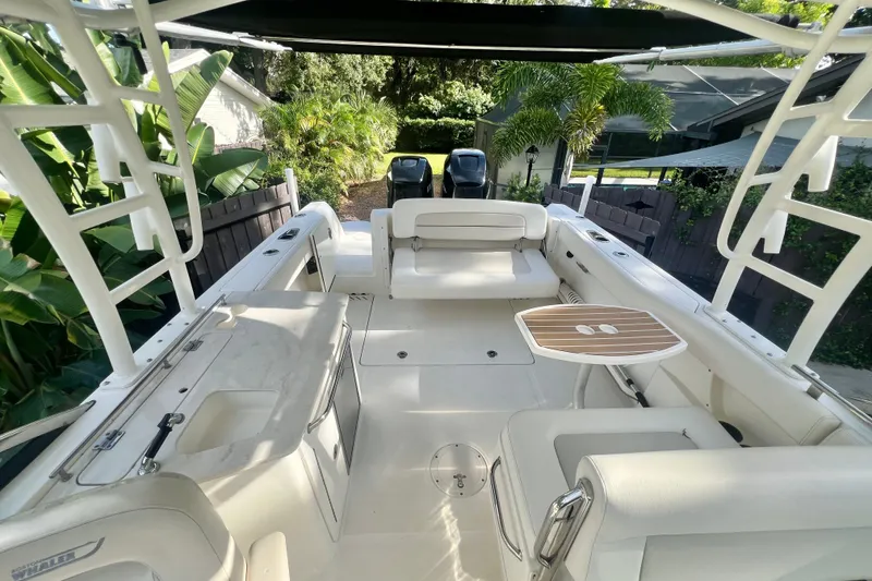 Slide: The Image of 2015 Boston Whaler 270 Vantage boat interior with seating and table, surrounded by lush greenery. - 54