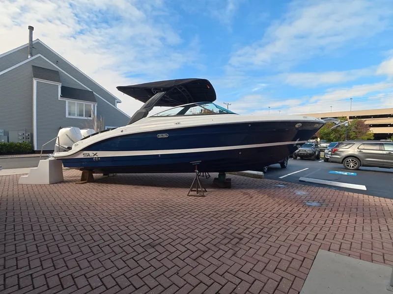 Slide: The Image of A 2027 Sea Ray SLX 280 Outboard is on a paved area, surrounded by buildings and cars. - 0