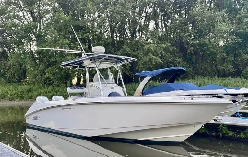 Slide: The Image of 2004 Boston Whaler 270 Outrage docked on a calm river with a wooded background. - 2