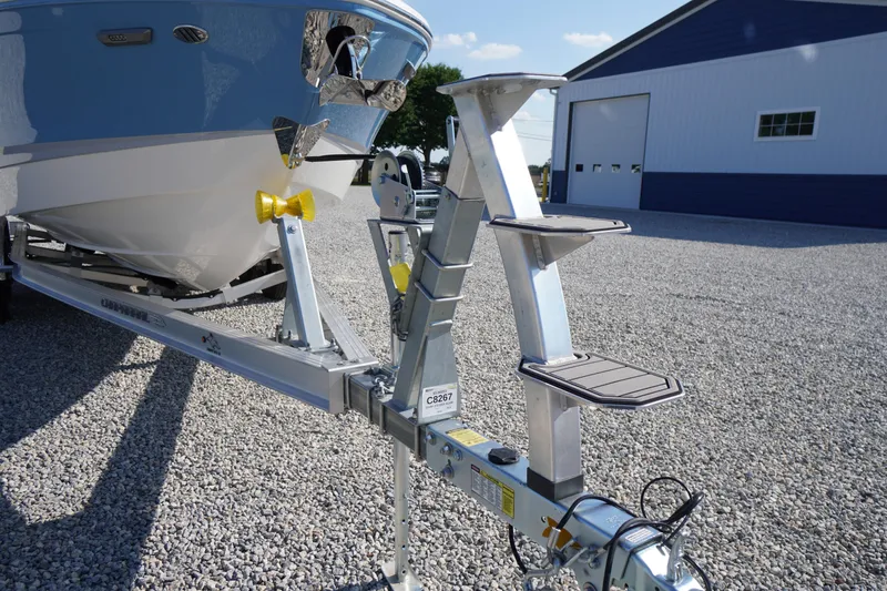 Slide: The Image of 2026 Chaparral 270 OSX boat on trailer, parked on gravel near a blue building. - 83