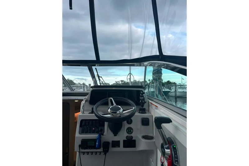 Slide: The Image of 2021 Regal 28 Express boat helm with steering wheel and controls, docked under cloudy sky. - 35