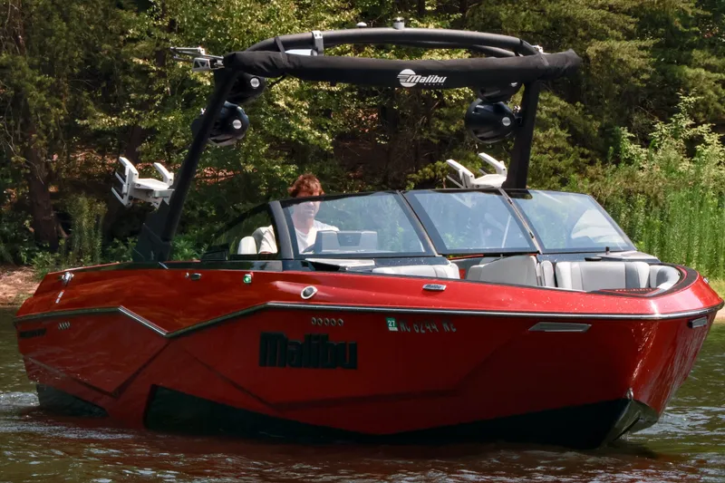 Slide: The Image of 2023 Malibu Wakesetter 25 LSV boat cruising on a lake with lush greenery. - 9