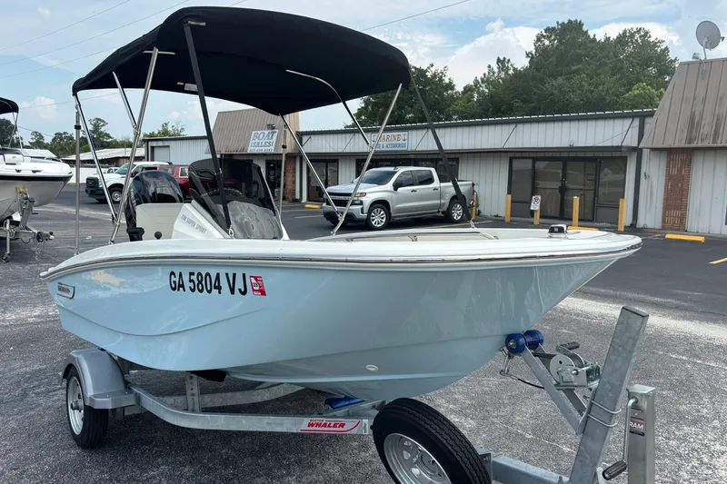 Slide: The Image of 2025 Boston Whaler 130 Super Sport boat on trailer, parked outside a marine store. - 4