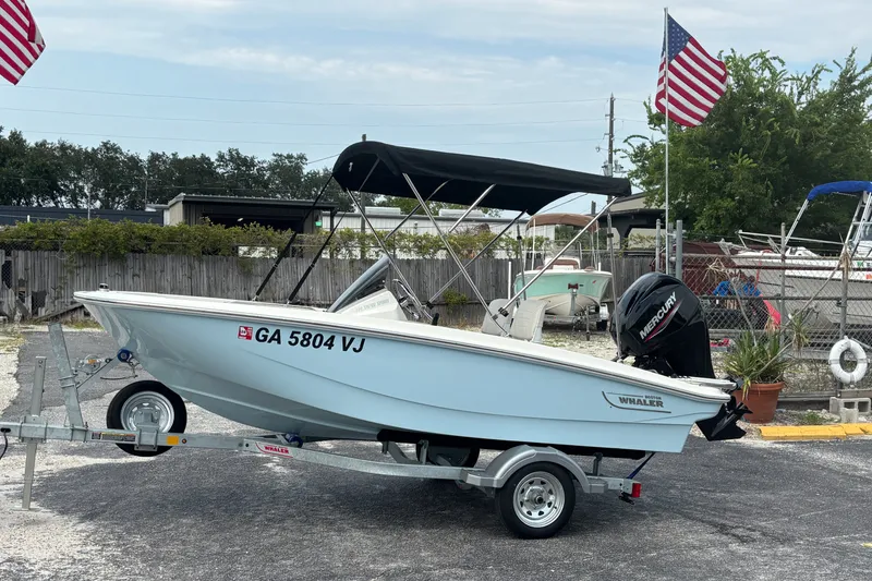 The Image of 2025 Boston Whaler 130 Super Sport boat on trailer, parked with American flags in background. - 0