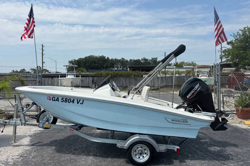 Slide: The Image of 2025 Boston Whaler 130 Super Sport boat on trailer, with Mercury engine, parked outdoors. - 9