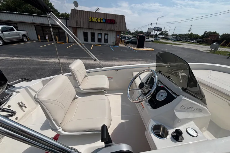 Slide: The Image of 2025 Boston Whaler 130 Super Sport boat interior with steering wheel and seating, parked near a store. - 17