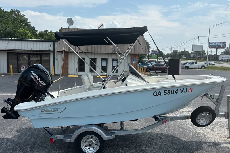 Slide: The Image of 2025 Boston Whaler 130 Super Sport boat on trailer, parked outdoors with Mercury engine. - 1
