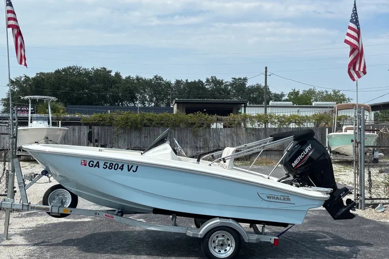 Slide: The Image of 2025 Boston Whaler 130 Super Sport boat on trailer, displayed outdoors with American flags. - 5