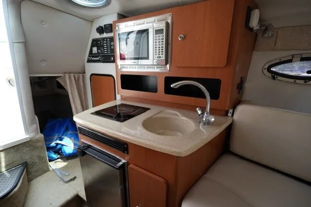 Slide: The Image of 2008 Crownline 250 CR boat interior with kitchenette, featuring microwave, sink, and compact fridge. - 18