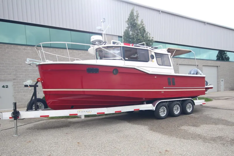 The Image of 2026 Ranger Tugs R-27 boat in red on a trailer outside a warehouse. - 1