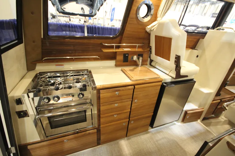 Slide: The Image of 2026 Ranger Tugs R-27 interior kitchen with stove, sink, and compact fridge. - 11