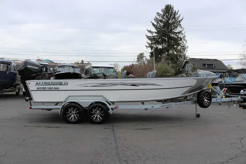 The Image of 2027 Alumaweld Super Vee Pro 23 boat on trailer, side view in outdoor setting. - 1