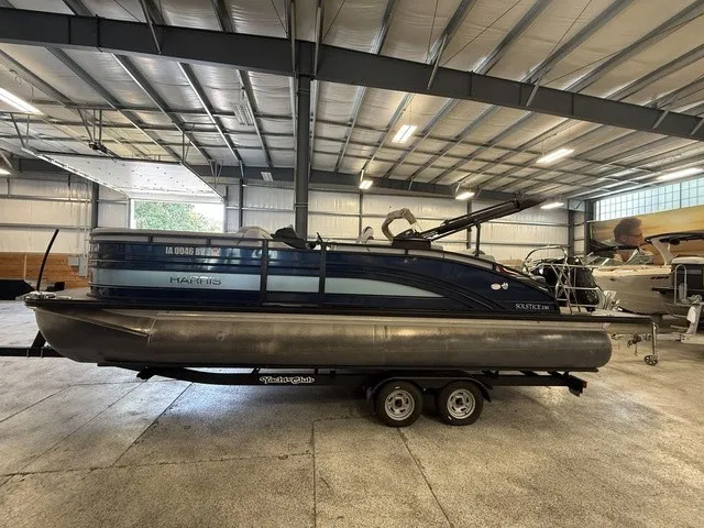 Slide: The Image of A 2021 Harris Solstice 250 SLDH pontoon boat on a trailer in a warehouse. - 2