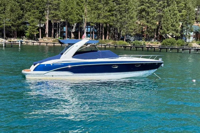 The Image of 2008 Formula 310 Sun Sport boat on a serene lake with forested shoreline. - 0