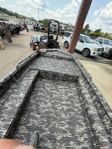 Slide: The Image of A 2026 Havoc 1756 MSTC boat with camouflage pattern, parked next to a tractor and cars. - 27