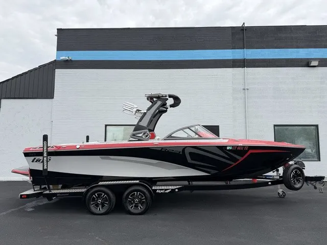 The Image of A 2018 Tigé R23 boat on a trailer, featuring a black and red design, in front of a building. - 1