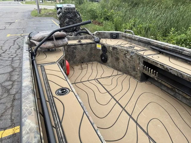 Slide: The Image of The image shows an Excel 175 SWF4 Legacy boat from 2026. It features a camouflage-patterned deck and open seating arrangement. The boat is parked on a lot beside a road, surrounded by grass. - 6