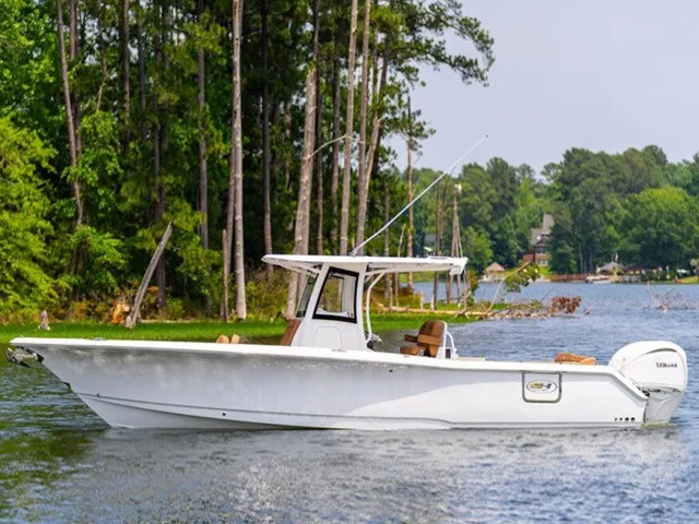 The Image of A white 2027 Sea Hunt Ultra 305 FS boat on a calm lake, surrounded by trees. - 1