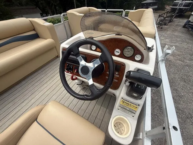 Slide: The Image of The image shows the helm of a 2002 Harris Sunliner 220 pontoon boat with a black steering wheel and beige upholstery. - 9