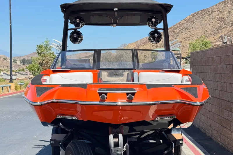 Slide: The Image of 2018 Malibu Wakesetter 22 MXZ boat, vibrant orange, parked on a trailer, mountainous backdrop. - 2